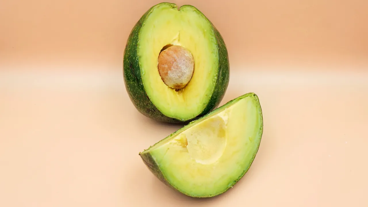Połówka awokado z pestką i kawałek obok. Czy adwokat może się zepsuć? To pytanie, na które odpowiedź znajdziemy, gdy owoc będzie zbyt dojrzały.