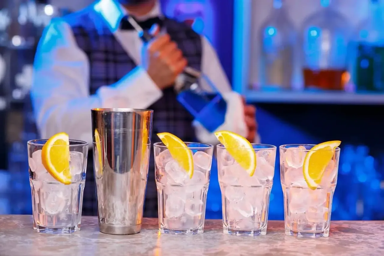 Barman przygotowuje drinki. Zastanawiasz się, ile kosztuje kurs na barmana? Zobacz, jak powstają drinki z lodem i pomarańczą.