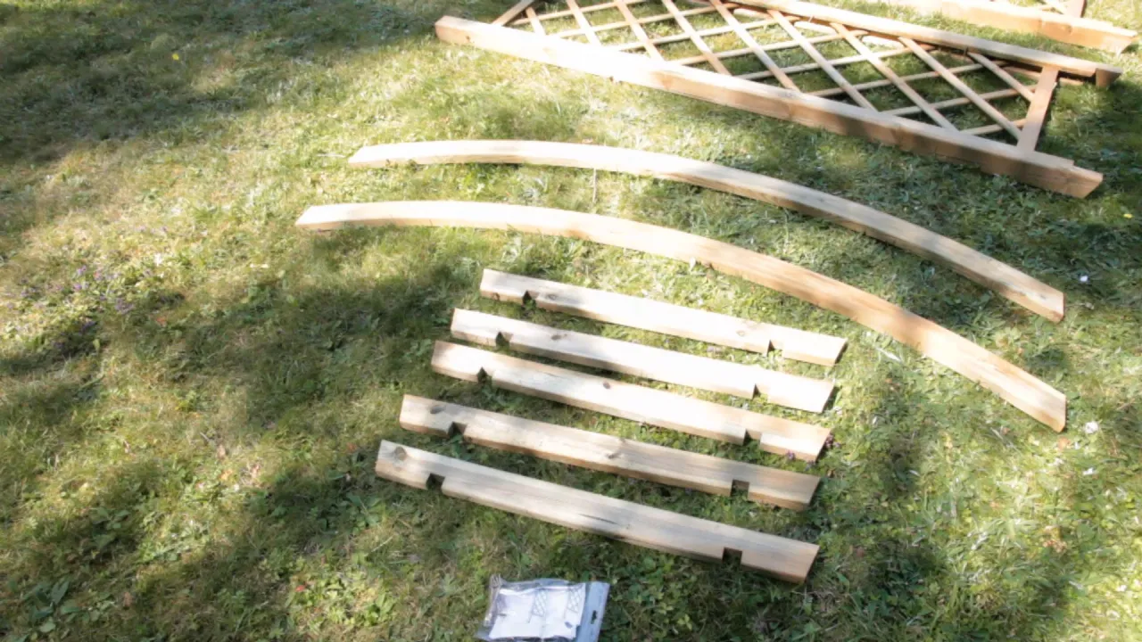 Drewniane elementy do budowy pergoli lamelowej jak zrobić. Widać łuki, deski i kratownicę na trawie.