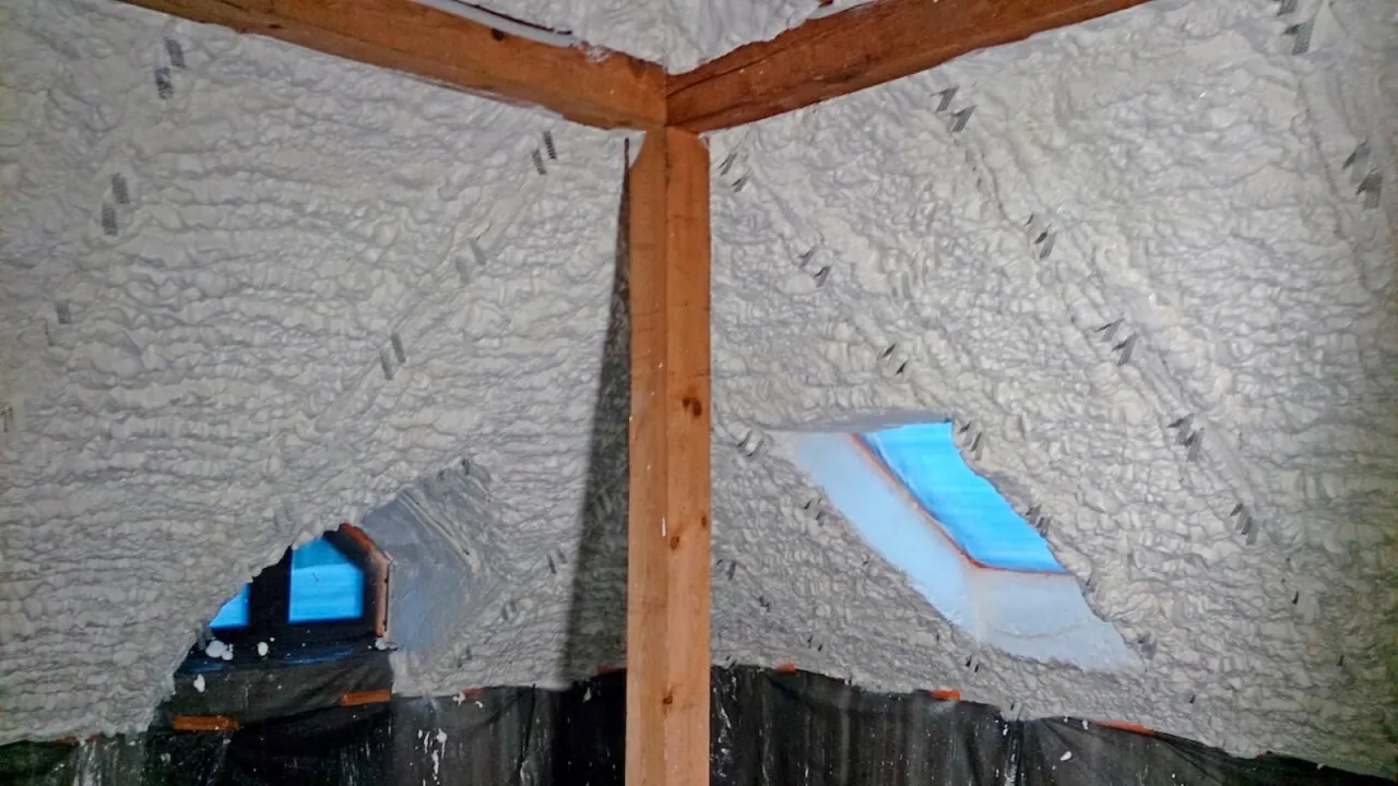 Pianka poliuretanowa na skosach poddasza to sposób, jak ocieplić skosy na poddaszu. Widać drewniane belki i okna dachowe.