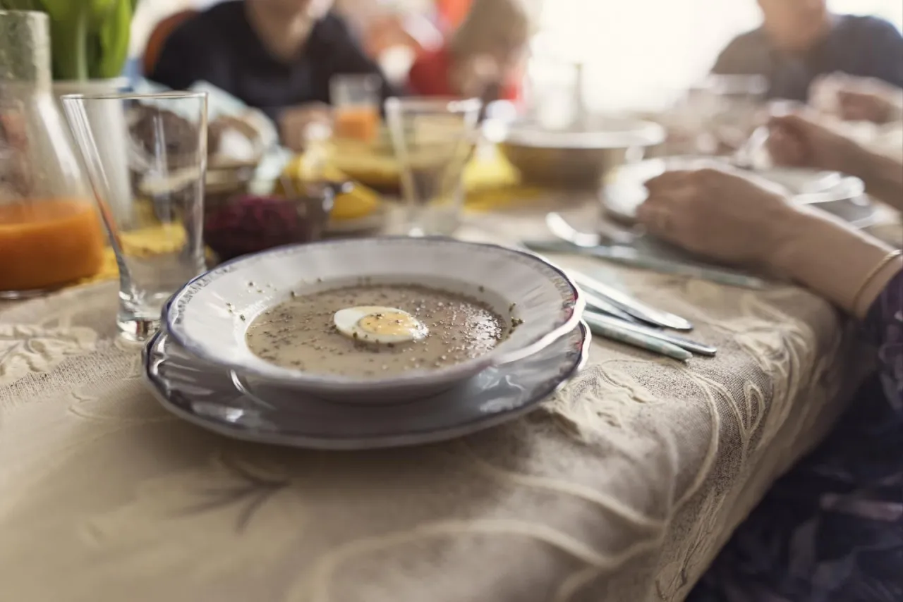 Rodzinny obiad. Na stole talerz z żurkiem na zakwasie lub barszczem białym, ozdobiony połówką jajka.