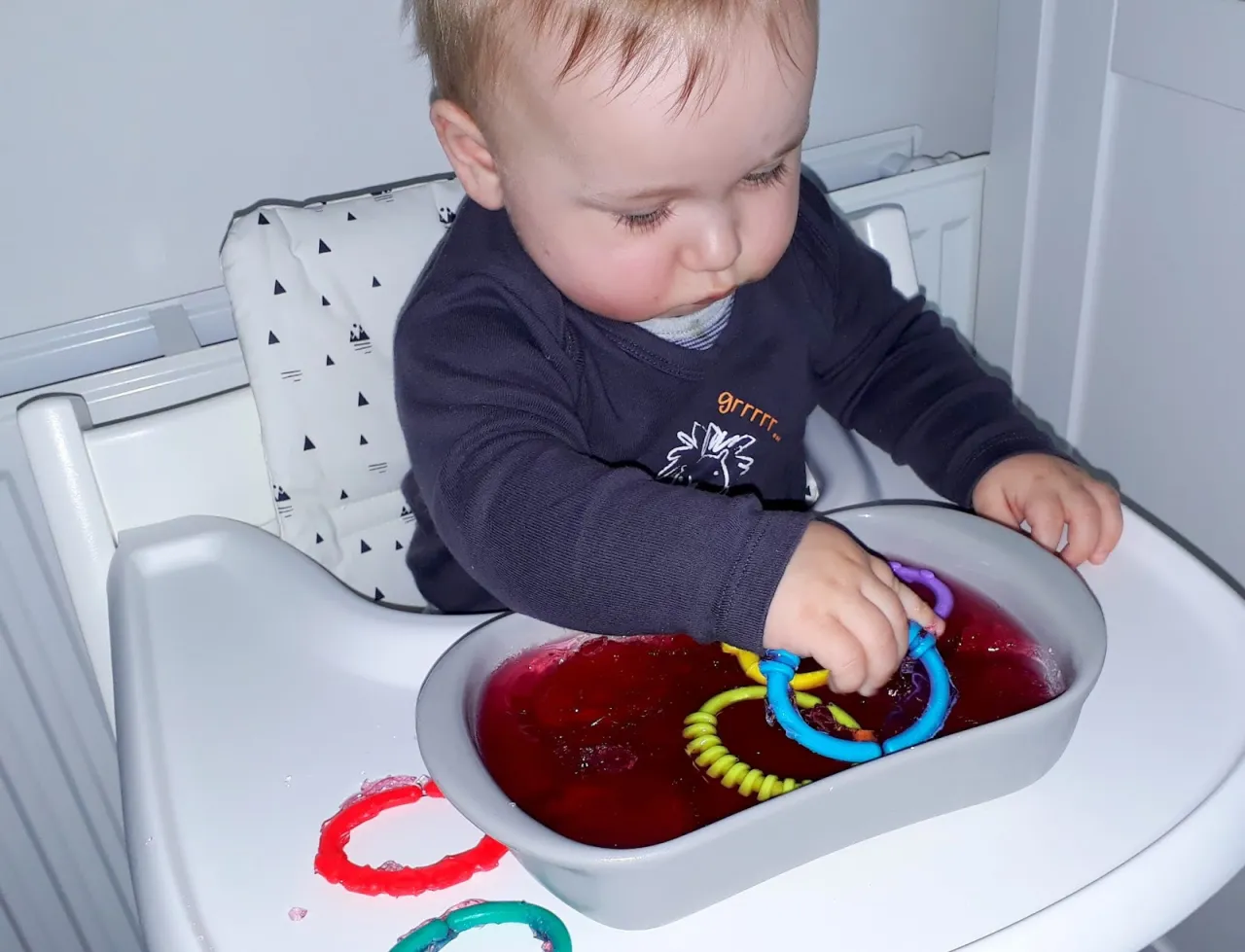 Dziecko bawi się galaretką sensoryczną, uśmiechnięte, z zabawkami w galaretce