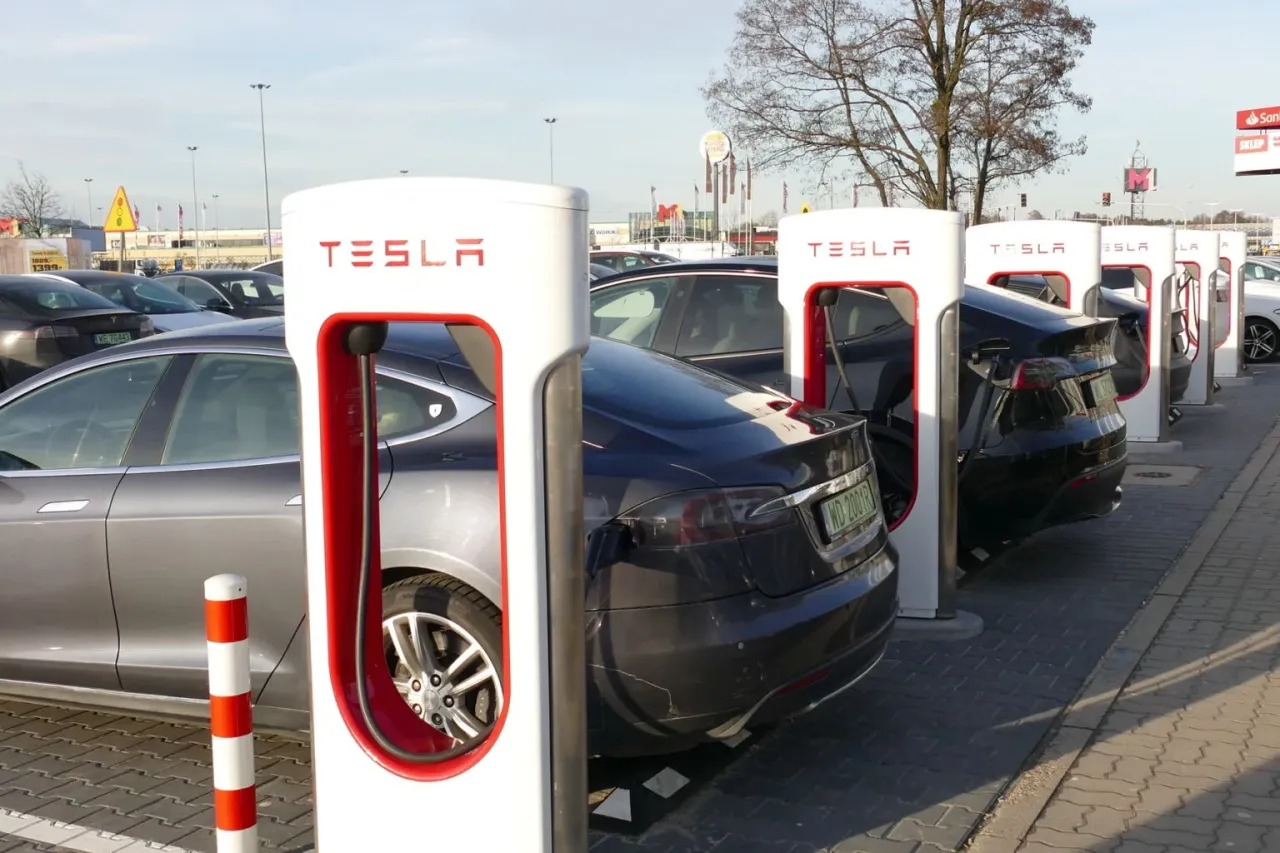 Rząd Tesli na ładowarce. Zastanawiasz się tesla co to? To elektryczne samochody, kt&oacute;re tu właśnie czerpią energię.