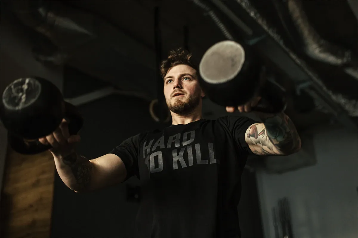 Mężczyzna z tatuażami ćwiczy z kettlebellami. Czy to crossfit czy siłownia, liczy się trening!
