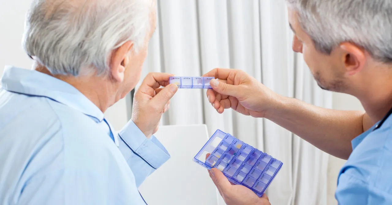 Opiekun pokazuje seniorowi pojemnik na leki. Czy leki dla seniorów są za darmo? To pytanie nurtuje wielu.