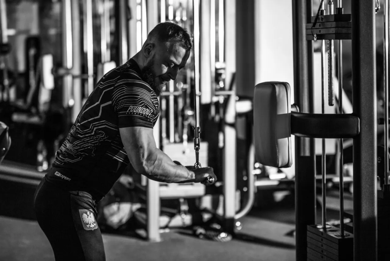Mężczyzna ćwiczący na siłowni z użyciem wyciągu.