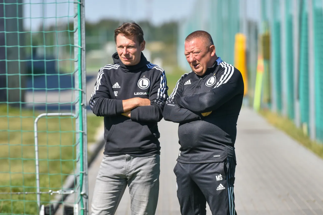 Dw&oacute;ch mężczyzn w dresach Legii, z rękami skrzyżowanymi na piersi, stoi przy bramce. Może to być lekcja, jak nie być profesjonalnym piłkarzem.