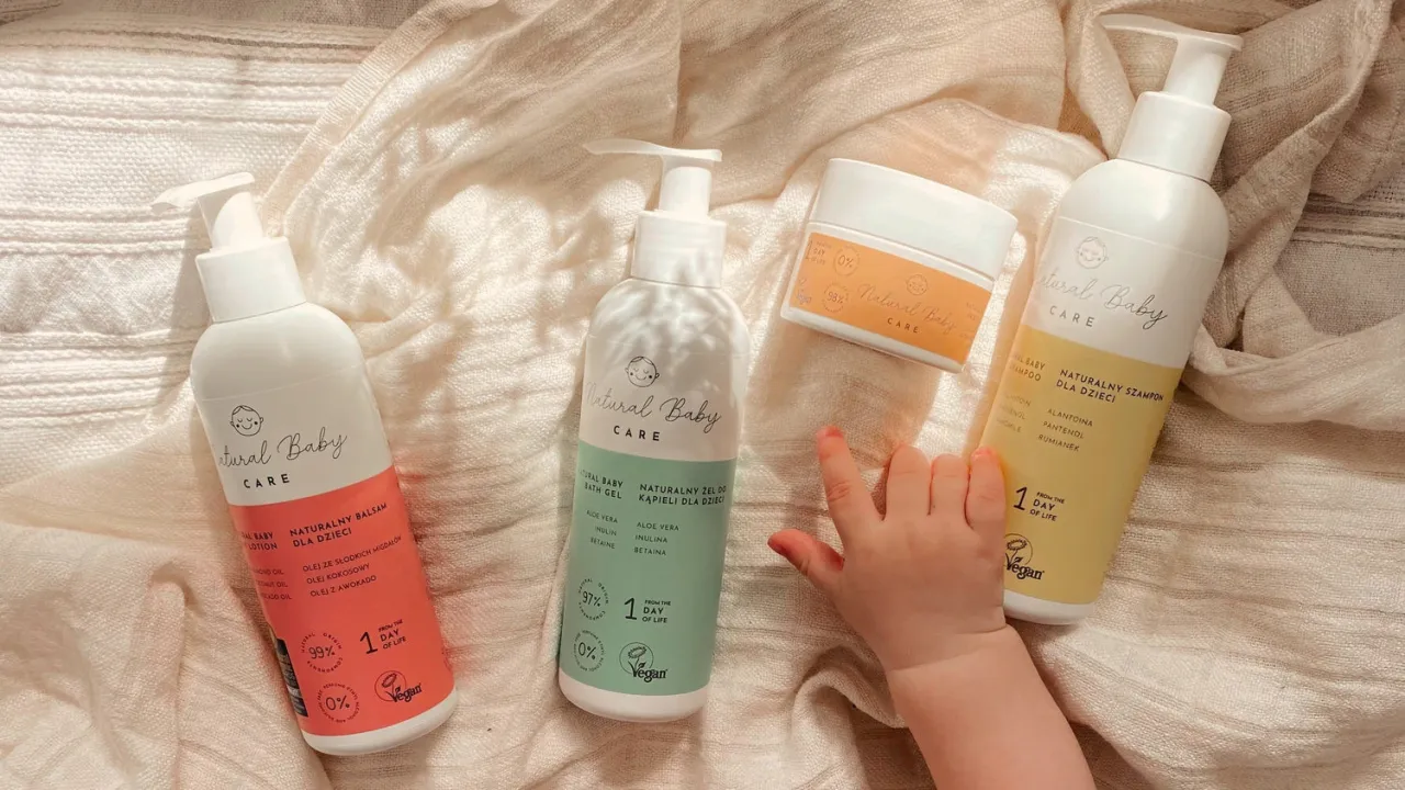 Naturalne kosmetyki dla noworodka: balsam, żel do kąpieli i szampon. Dziecięca rączka sięga po nie.