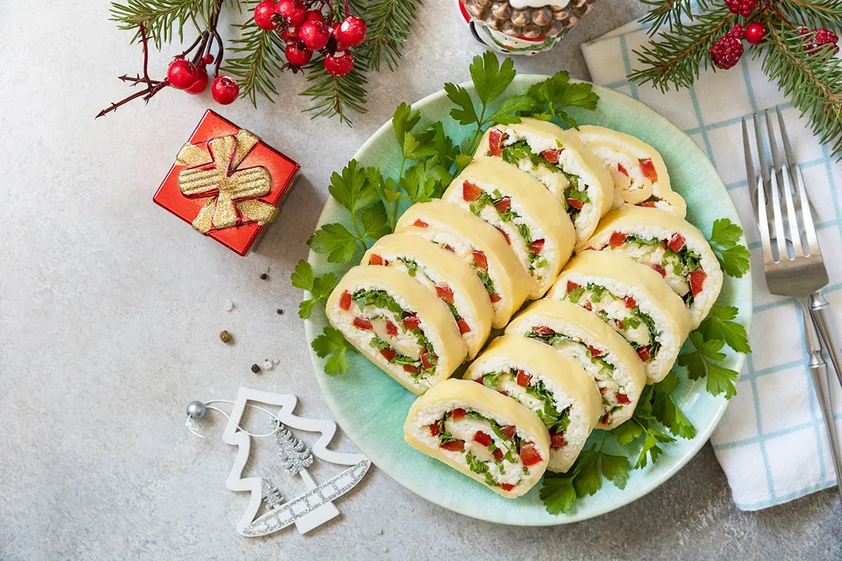 Roladki z sera z papryką i ziołami na talerzu, idealne jako inspiracja, co ugotować na Wigilię. Obok świąteczne dekoracje.