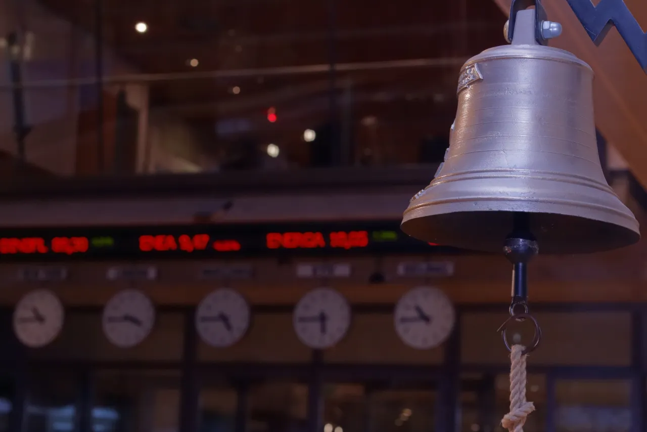 Dzwon na giełdzie papier&oacute;w wartościowych co to? W tle zegary i kursy akcji.