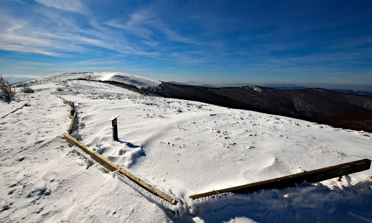 Zimowe szlaki w Bieszczadach otwarte, pokryte śniegiem, z drewnianymi balustradami i tabliczką informacyjną.