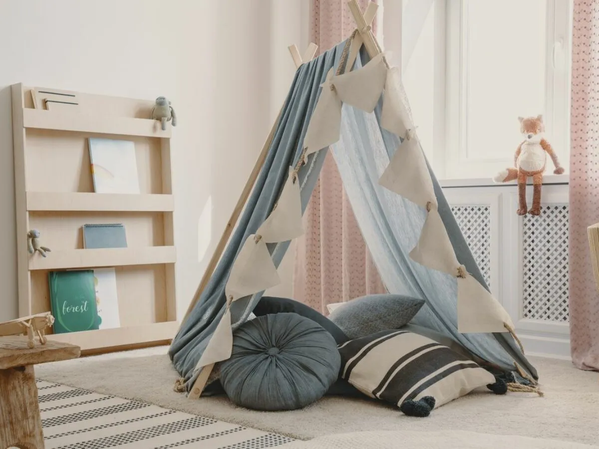 Dziecięcy namiot tipi z poduszkami, idealny pomysł, jak zrobić bazę w domu. Na półce książki i zabawki.