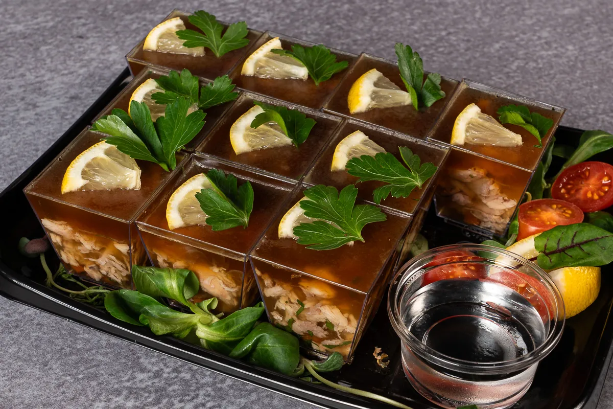 Galaretka z nóżek wieprzowych (przednich lub tylnych) w małych porcjach, ozdobiona cytryną i natką pietruszki.