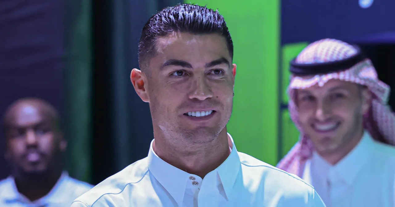 Uśmiechnięty Cristiano Ronaldo w białej koszuli, obok mężczyzny w tradycyjnym nakryciu głowy. Ciekawość budzi, ile zarabia Ronaldo.