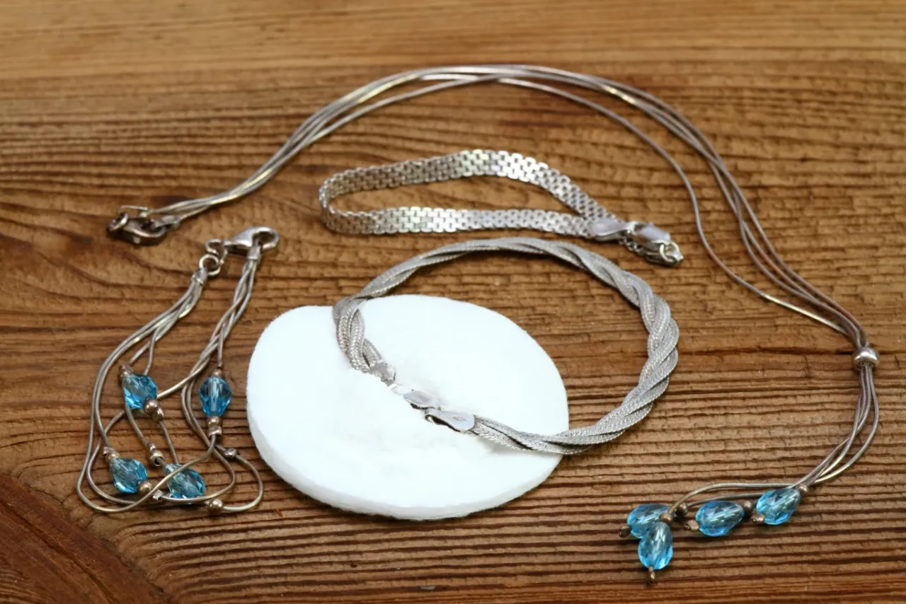 Srebrna biżuteria, w tym naszyjniki i bransoletki, leży na drewnianym tle. Zastanawiasz się, dlaczego srebro czernieje? To naturalny proces.