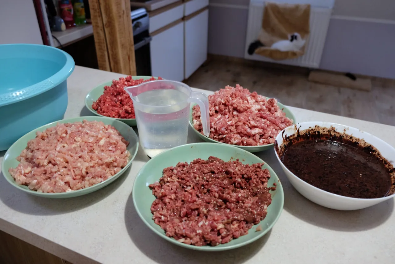 Na stole przygotowane są porcje mielonych serc drobiowych dla kota, obok dzbanek z wodą i miska z ciemną masą.