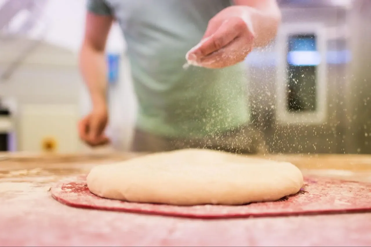 Ręka sypie mąkę na ciasto, pokazując, jak zrobic pizza.