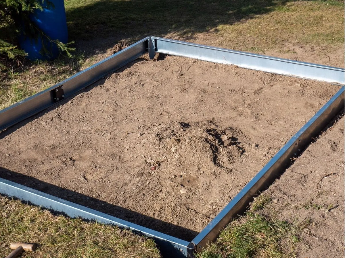 Metalowa rama na ziemi, gotowa na zrobienie fundamentu pod szklarnię.