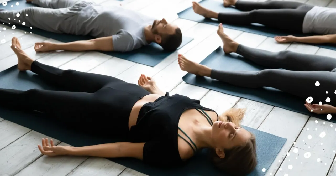 Grupa osób leży na matach, wykonując ćwiczenia jogi nidra. Relaks i głęboki oddech.