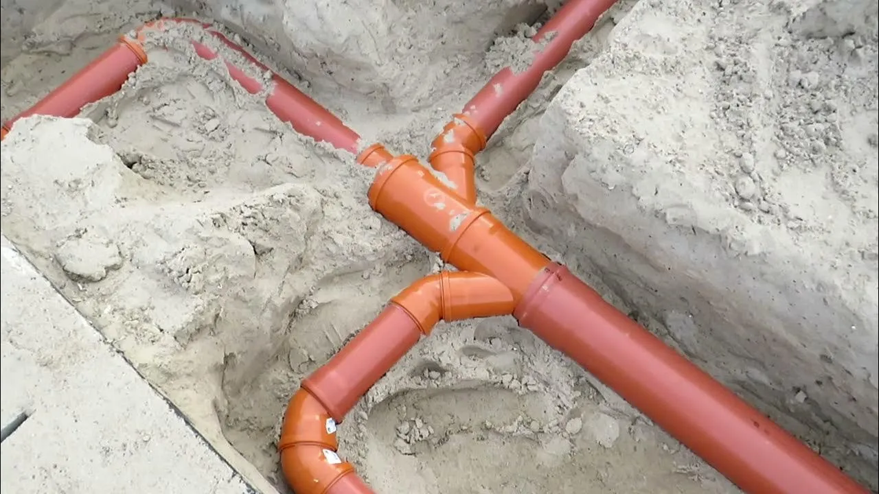 układanie pomarańczowej rury kanalizacyjnej w wykopie pod podjazdem samochodowym