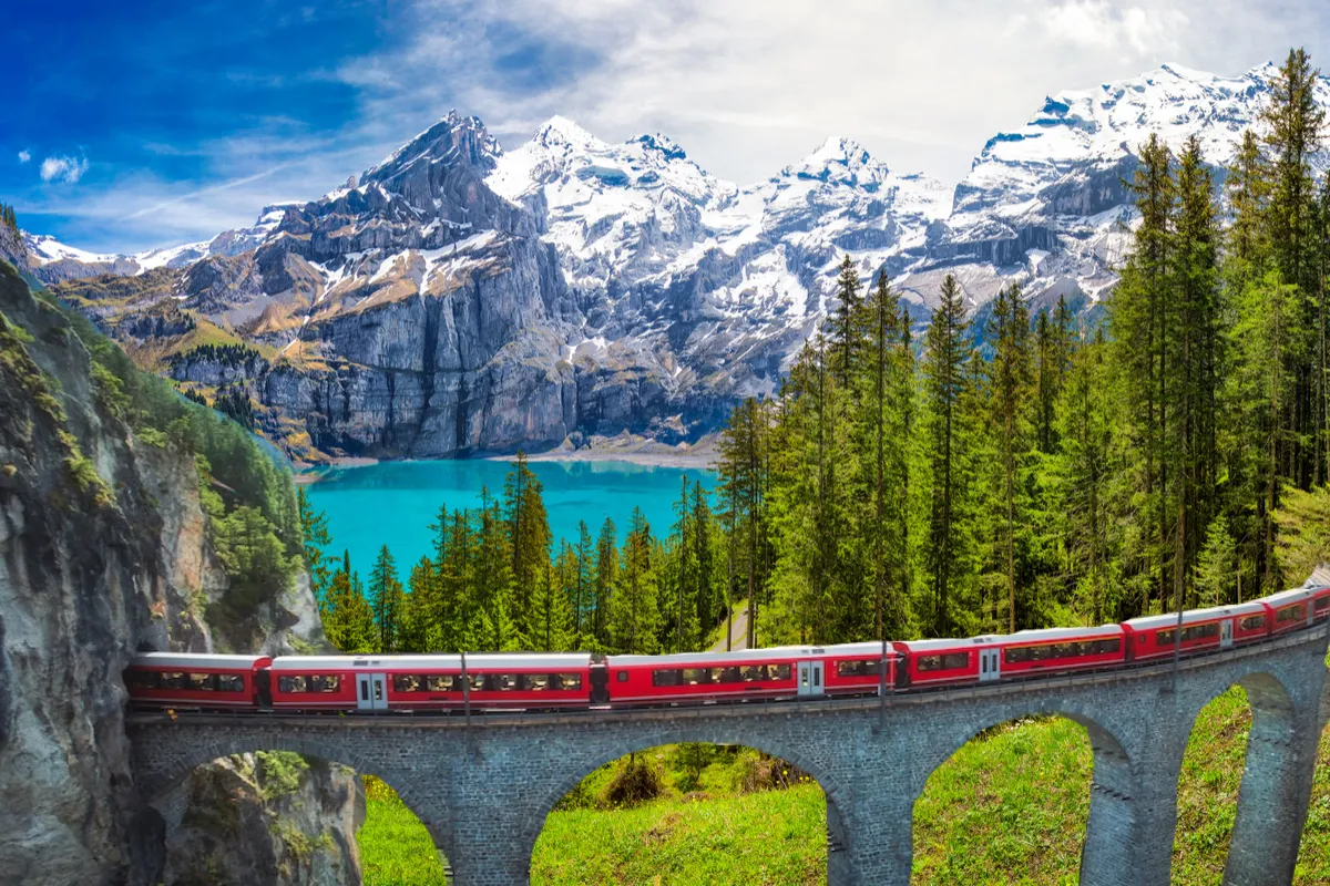 Czerwony pociąg przemierza malownicze Alpy Szwajcarskie, gdzie jechać, by podziwiać turkusowe jezioro i ośnieżone szczyty.