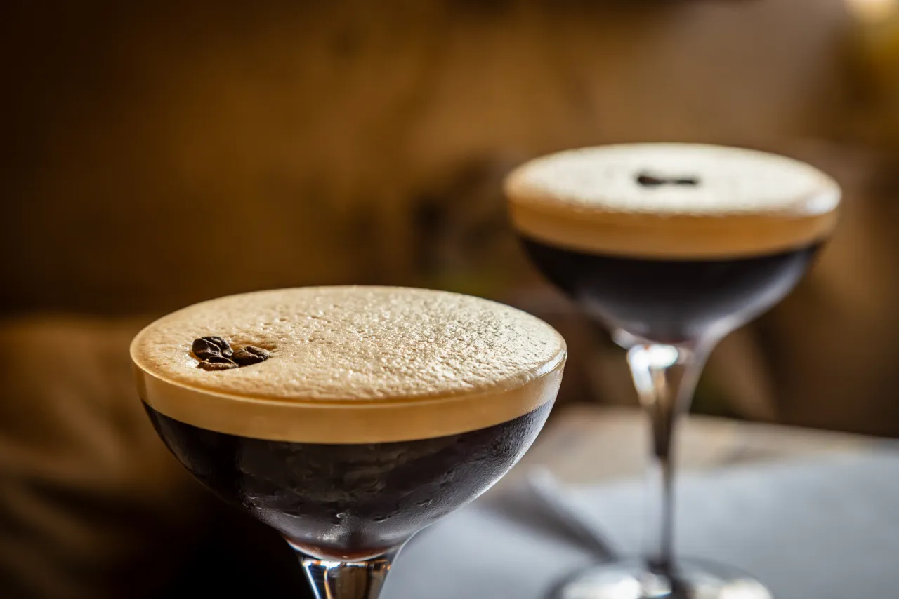 Dwa drinki z pianką i ziarnami kawy. Wybór między Espresso Martini a Irish Coffee.