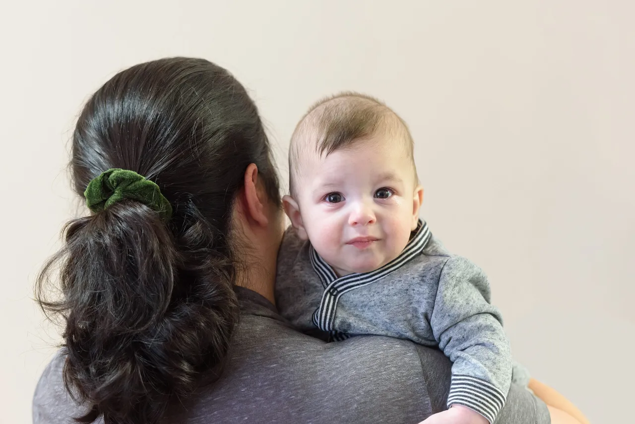 Dziecko na ramieniu mamy, z zaciekawieniem patrzy w obiektyw. Czas szybko leci, a do którego roku życia się rośnie?
