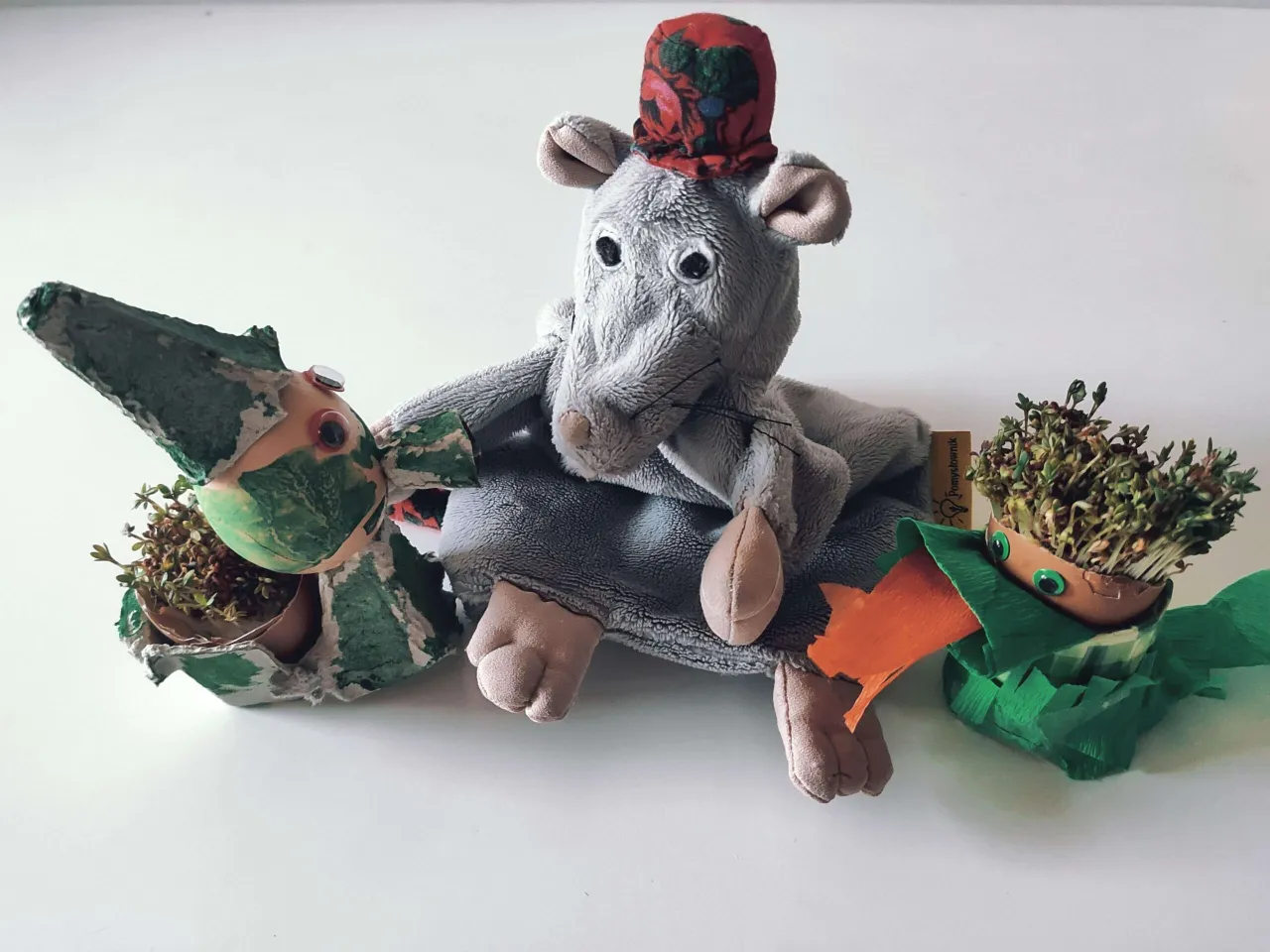 Pluszowa myszka w czapce z kwiatami i dwie kreatywne rzeżuchy w skorupkach jajek. Pomysły przedszkole na wiosenne dekoracje.