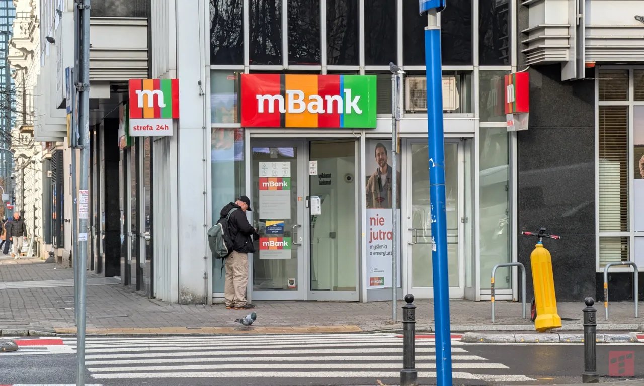 Przed plac&oacute;wką mBanku mężczyzna przy bankomacie. Chcesz wiedzieć, jak usunąć zaufane urządzenie mbank?