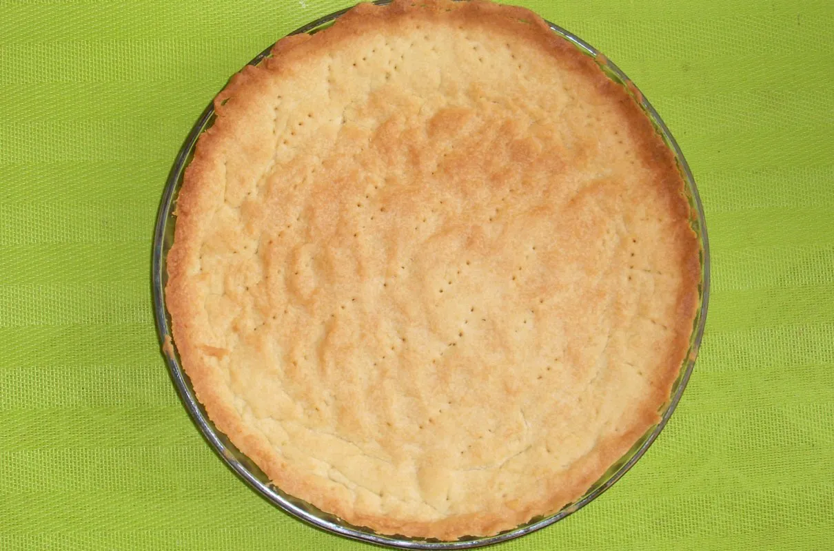 Złociste ciasto na tartę wytrawną, lekko zarumienione na brzegach, z widocznymi dziurkami, gotowe do wypełnienia ulubionym farszem.