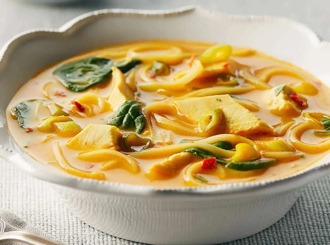 Aksamitny bulion z kurczakiem, makaronem i szpinakiem. Pyszne tajskie jedzenie w białej misce.