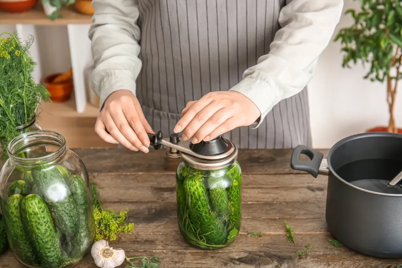 Przygotowanie ogórków do pasteryzowania w piekarniku. Słoik z ogórkami, koprem i czosnkiem jest zakręcany.