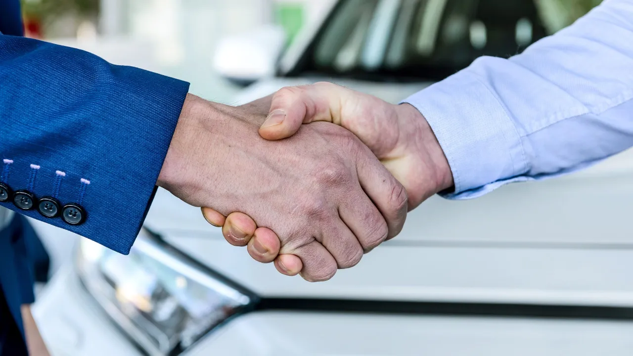 Uścisk dłoni po udanym zwrocie samochodu po zakupie. Nowy właściciel cieszy się z transakcji.