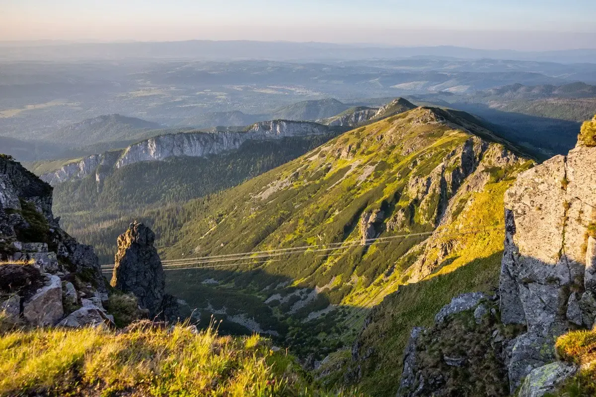 Widok na Tatry z Kasprowego Wierchu. Słońce oświetla zbocza, ukazując szlaki i skaliste grzbiety.