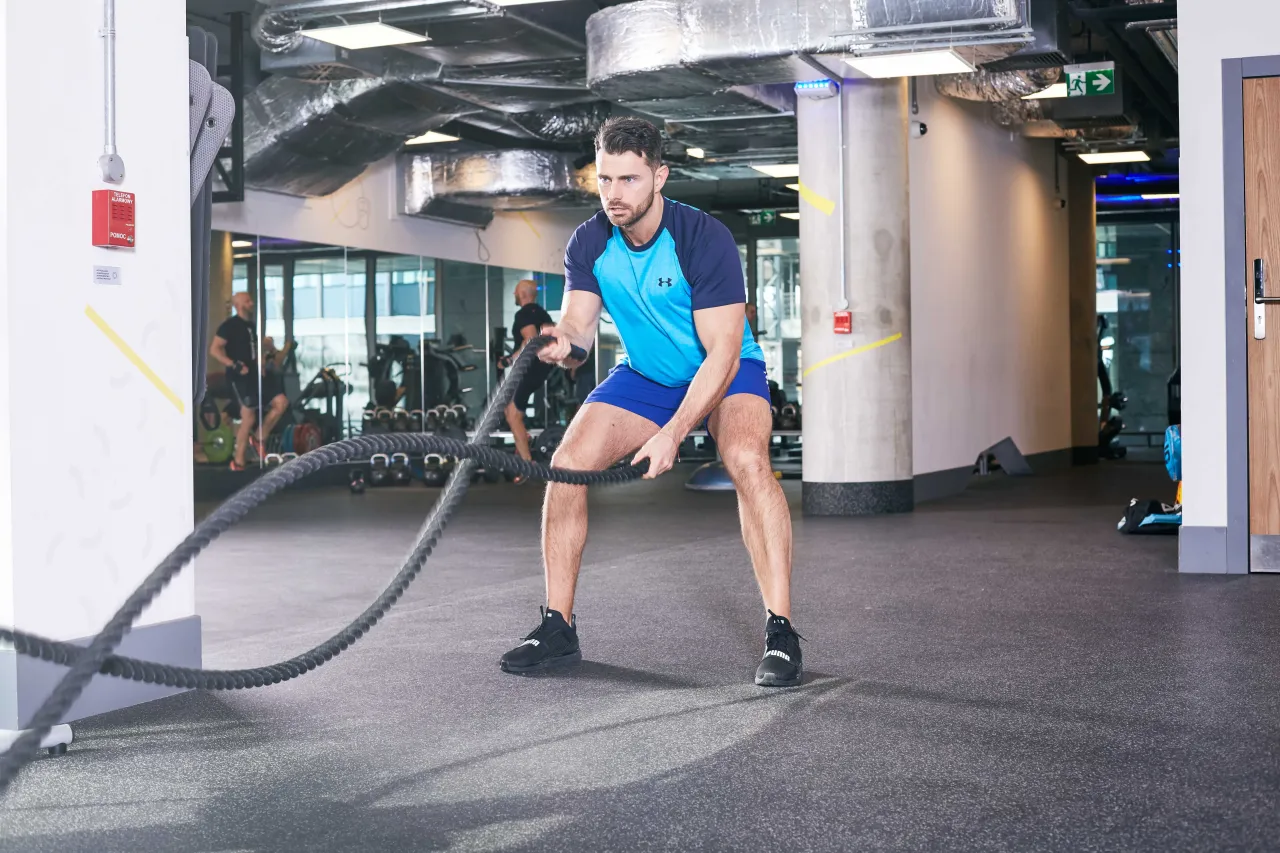 Mężczyzna ćwiczy z linami treningowymi. To świetny przykład, co to trening obwodowy &ndash; angażuje całe ciało i buduje siłę.