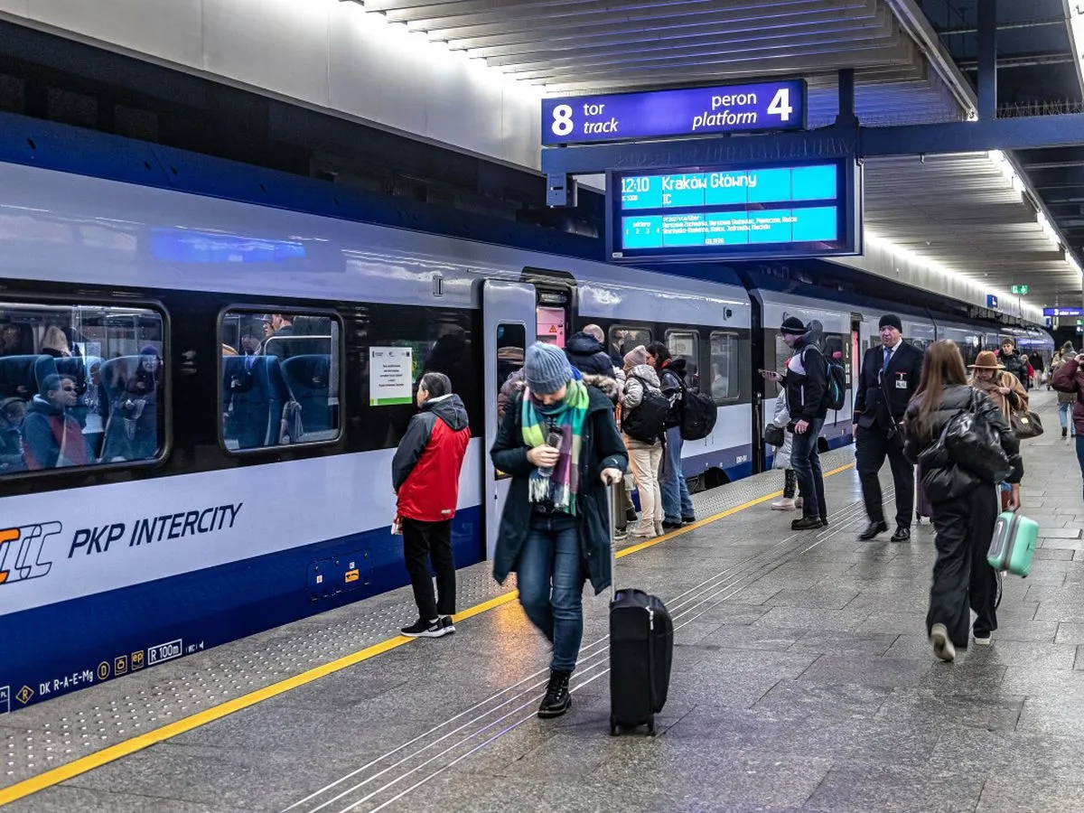 Na dworcu PKP Intercity ludzie z bagażami czekają na pociąg. Czy można kupić bilet w pociągu Intercity? Informacja na tablicy wskazuje odjazd do Krakowa Głównego.