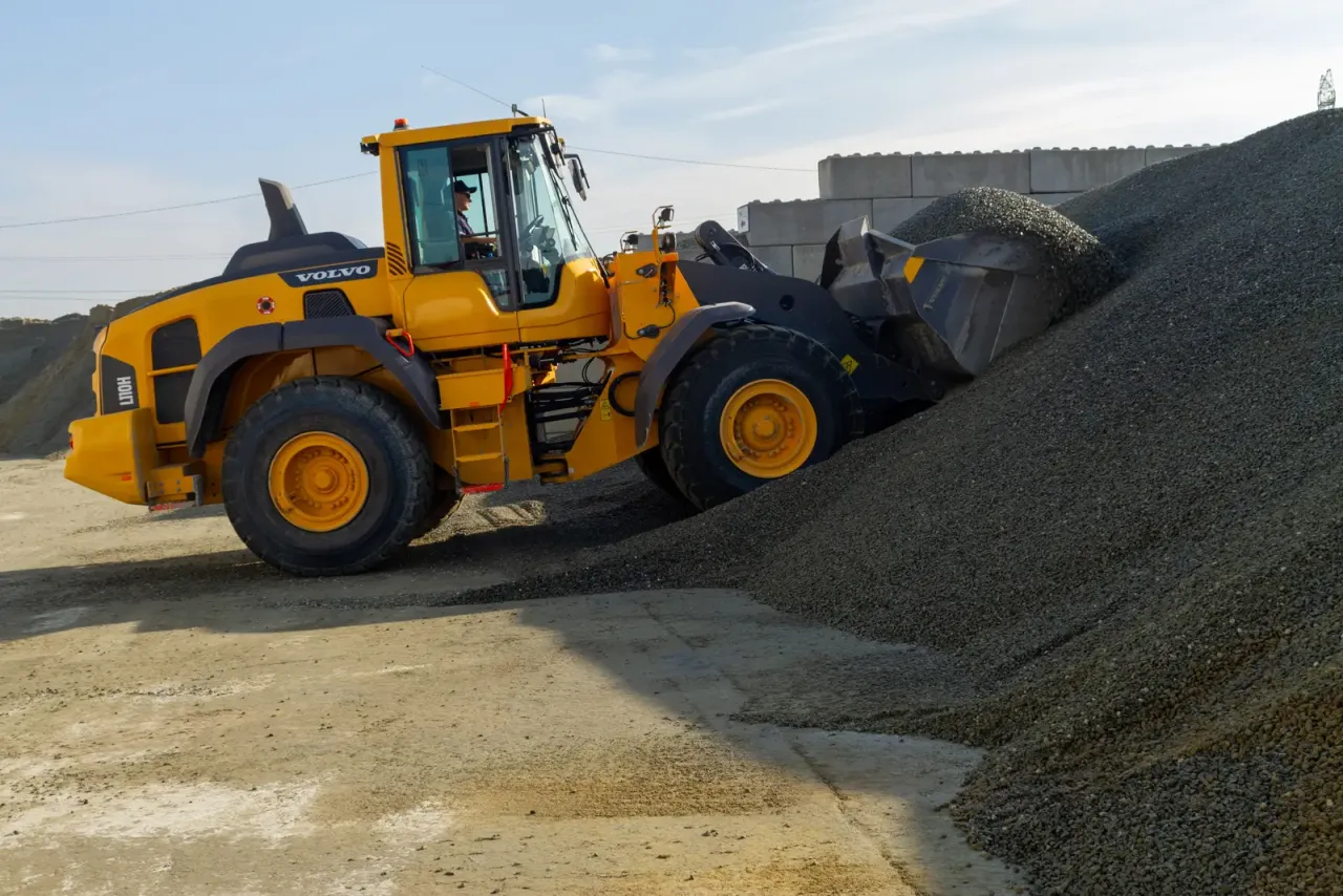 Ż&oacute;łta ładowarka Volvo nabiera kruszywo, kt&oacute;re posłuży do produkcji betonu. Warto wiedzieć, ile waży metr sześcienny betonu.