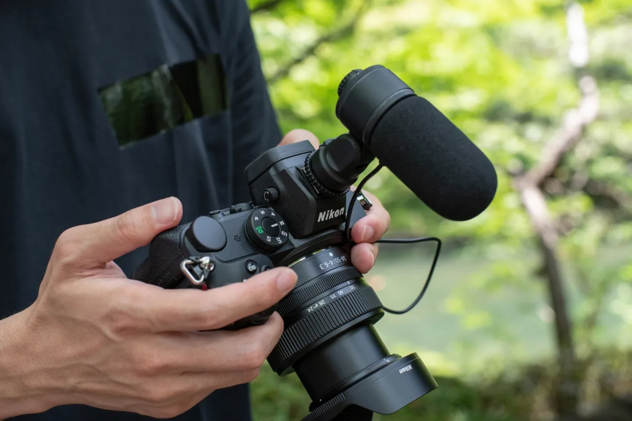 Ręce trzymające lustrzankę do vlogów z mikrofonem na gorącej stopce. Idealny sprzęt do tworzenia treści w plenerze.