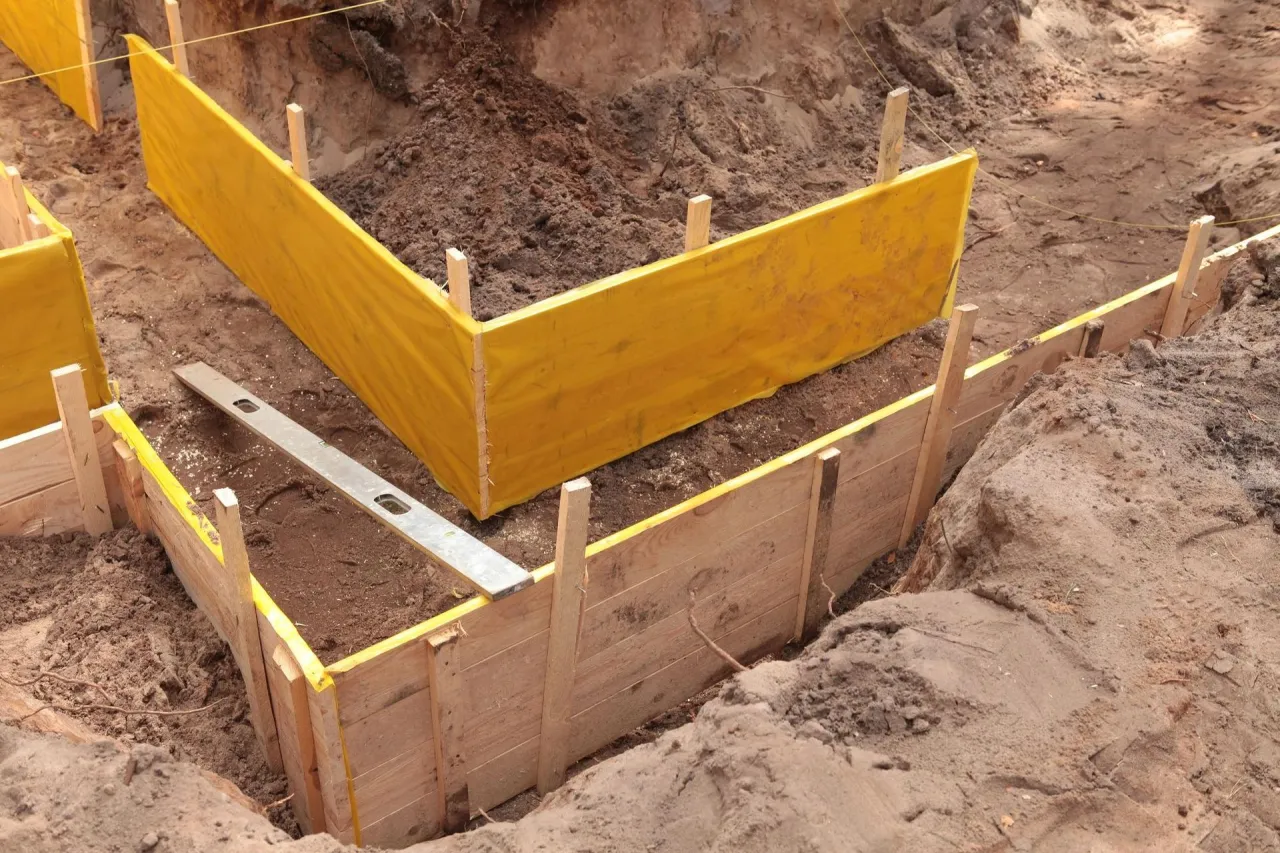 Drewniane szalunki z żółtą folią ochronną czekają na obsypanie fundamentów z zewnątrz.