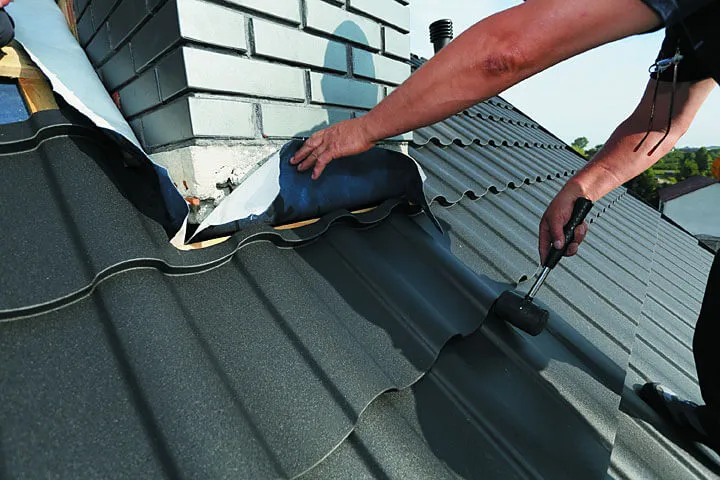 Dekarz naprawiający obróbkę blacharską komina