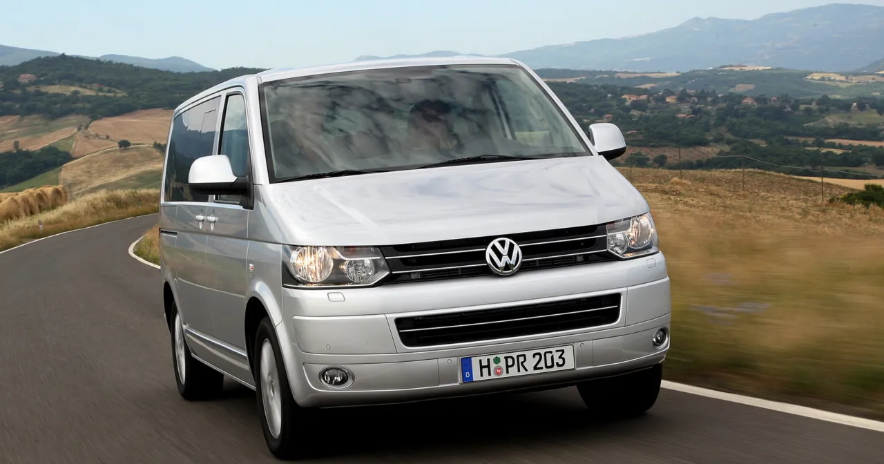 Srebrny Volkswagen Transporter na krętej drodze, idealny do akcje serwisowe vw. W tle malownicze wzg&oacute;rza Toskanii.