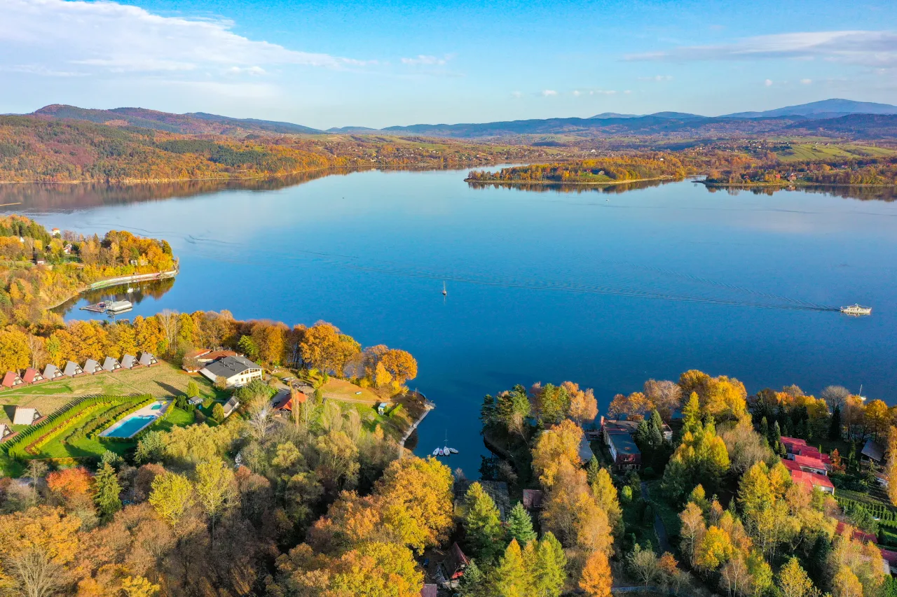 Jesienna panorama Jeziora Żywieckiego z łodziami i domkami. Idealne miejsce, by zobaczyć, co zwiedzić w Żywcu i okolicach.