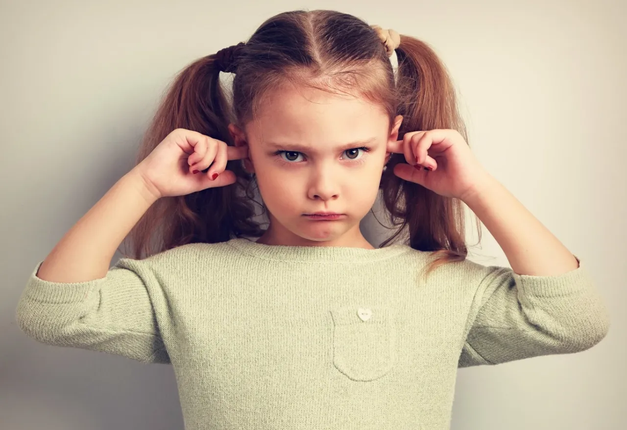 Dziecko zatykające uszy w hałaśliwym otoczeniu.