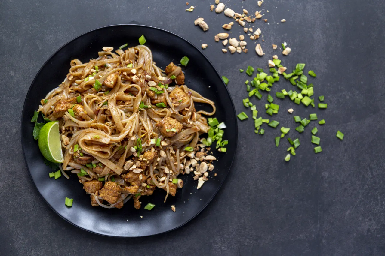 Pad Thai z kurczakiem, posypany orzeszkami ziemnymi i szczypiorkiem. Idealny przykład tajskich przepisów, który zachwyca smakiem.