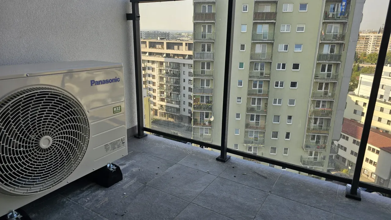 Jednostka zewnętrzna klimatyzacji Panasonic na balkonie, gotowa do montażu w bloku. Widok na sąsiednie budynki.