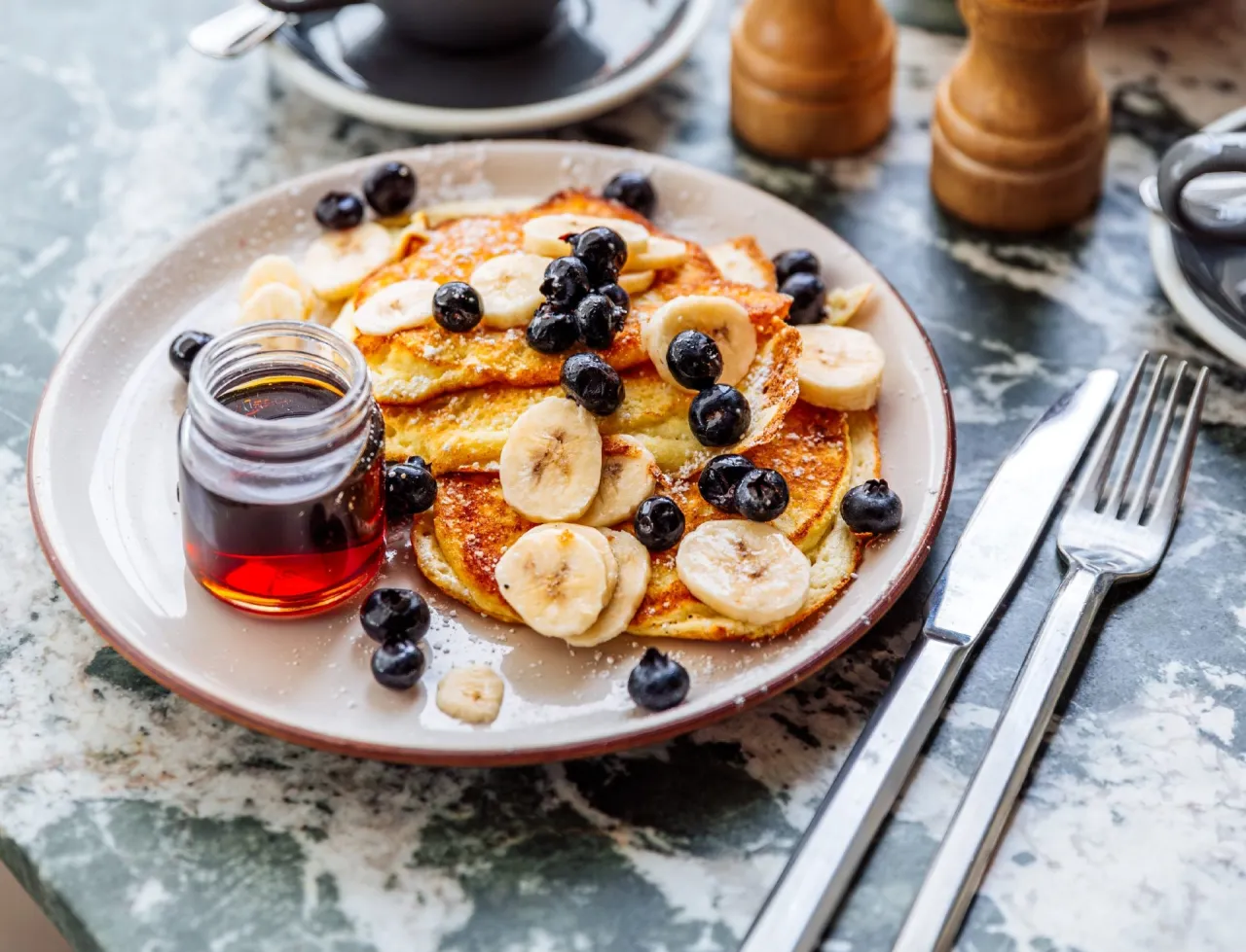 Pyszne, zdrowe pancakes z bananem i bor&oacute;wkami, posypane cukrem pudrem. Idealne na śniadanie, jako inspiracja na przepis na zdrowe pancakes.