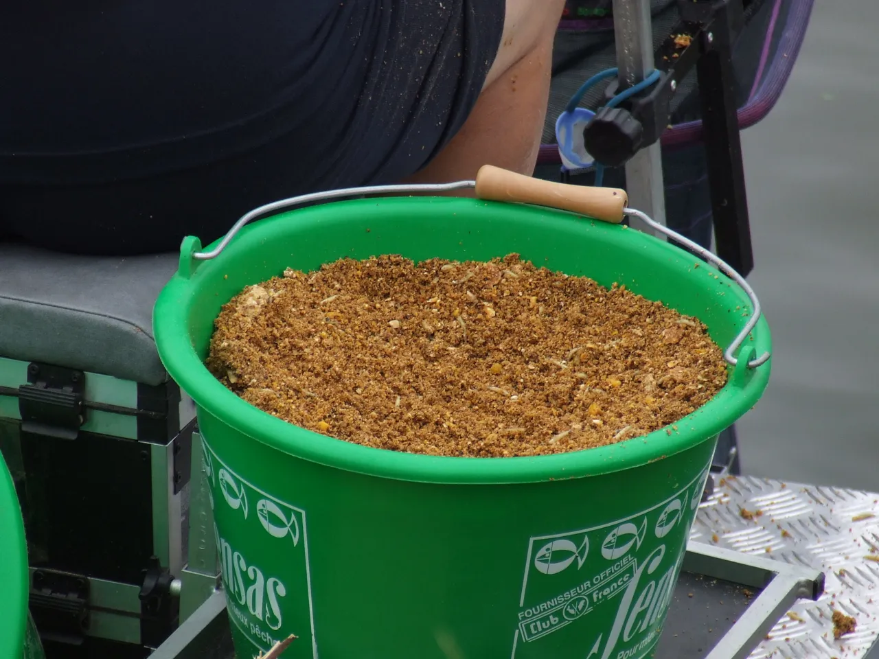 Zielone wiadro pełne zanęty na ryby, z widocznymi białymi robakami. Czy to zakazane zanęty na ryby?