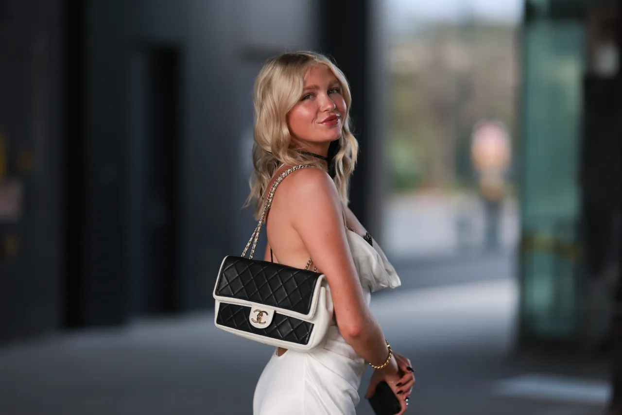 Elegancka blondynka w białej sukience i czarnej torebce Chanel, idealna na urodziny w lokalu.