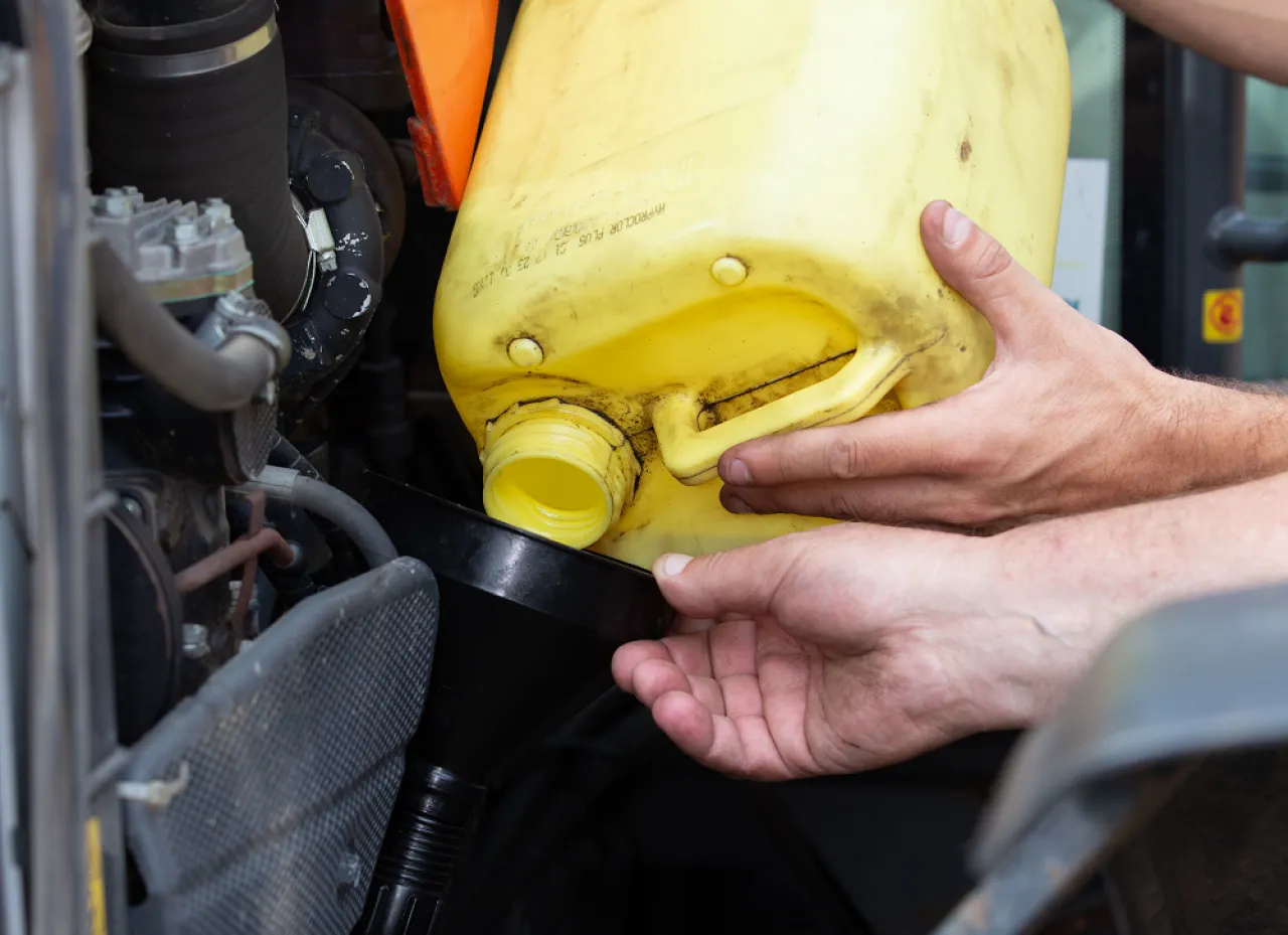 Dwie ręce przelewają płyn z żółtego kanistra do lejka, co jest częścią naprawy traktorków ogrodowych.