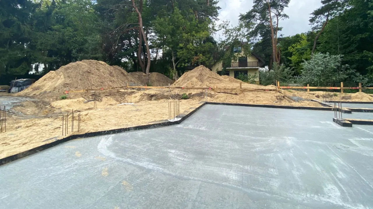 Plac budowy z betonową płytą fundamentową i hałdami piasku. Czekamy, aż ile muszą odstać fundamenty, zanim ruszą dalsze prace.